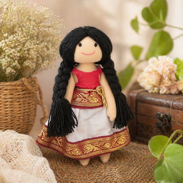 Doll in traditional outfit with braided hair, surrounded by flowers and a chest.