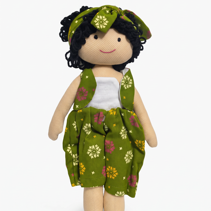 A handmade fabric doll with curly black yarn hair, wearing a green floral dress and matching headband over a white top, set against a plain white background.