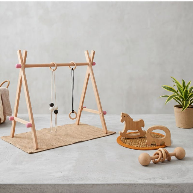 Wooden play gym and toys on a light gray floor with a plant in the background