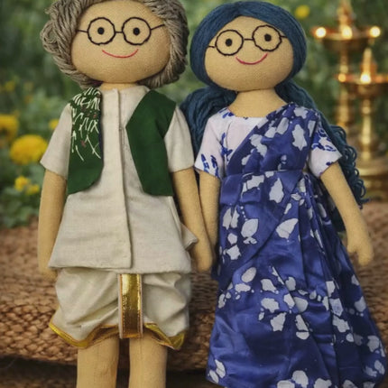  The Grandfather: Dressed in a classic cream dhoti-kurta with a gold-bordered trim and a stylish forest green Nehru jacket.

The Grandmother: Draped in a stunning indigo blue and white patterned saree with elegant folds.

Tactile & High Quality: Made from textured natural fabrics that feel sturdy yet soft, perfect for display or gentle p